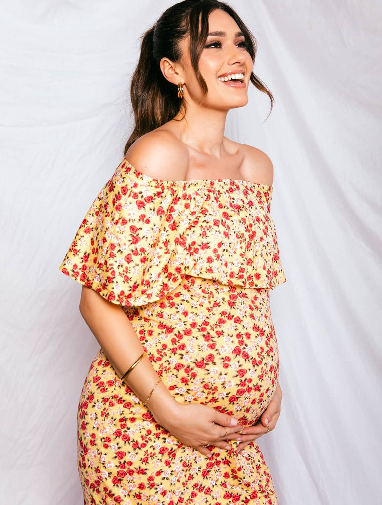 Pregnant mother smiling while wearing bright yellow and red floral maternity dress with white background