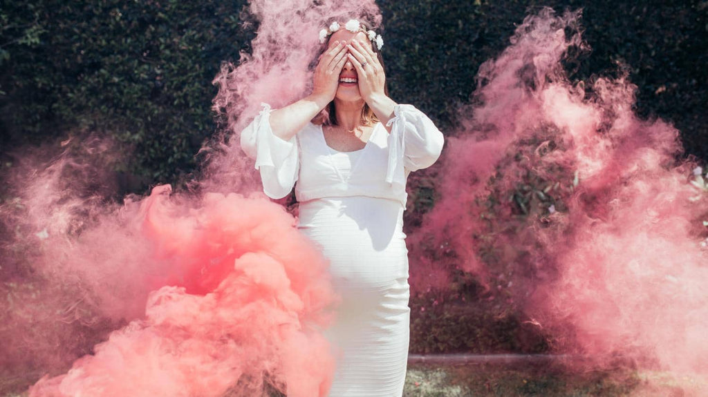 Pregnant mother wearing a white gender reveal pregnancy dress with pink smoke effects
