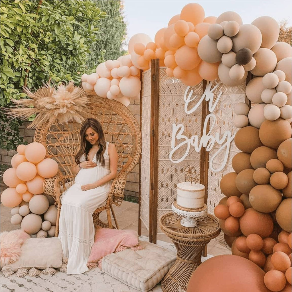 Pregnant mom wearing a white baby shower maternity dress sitting at fall themed baby shower party